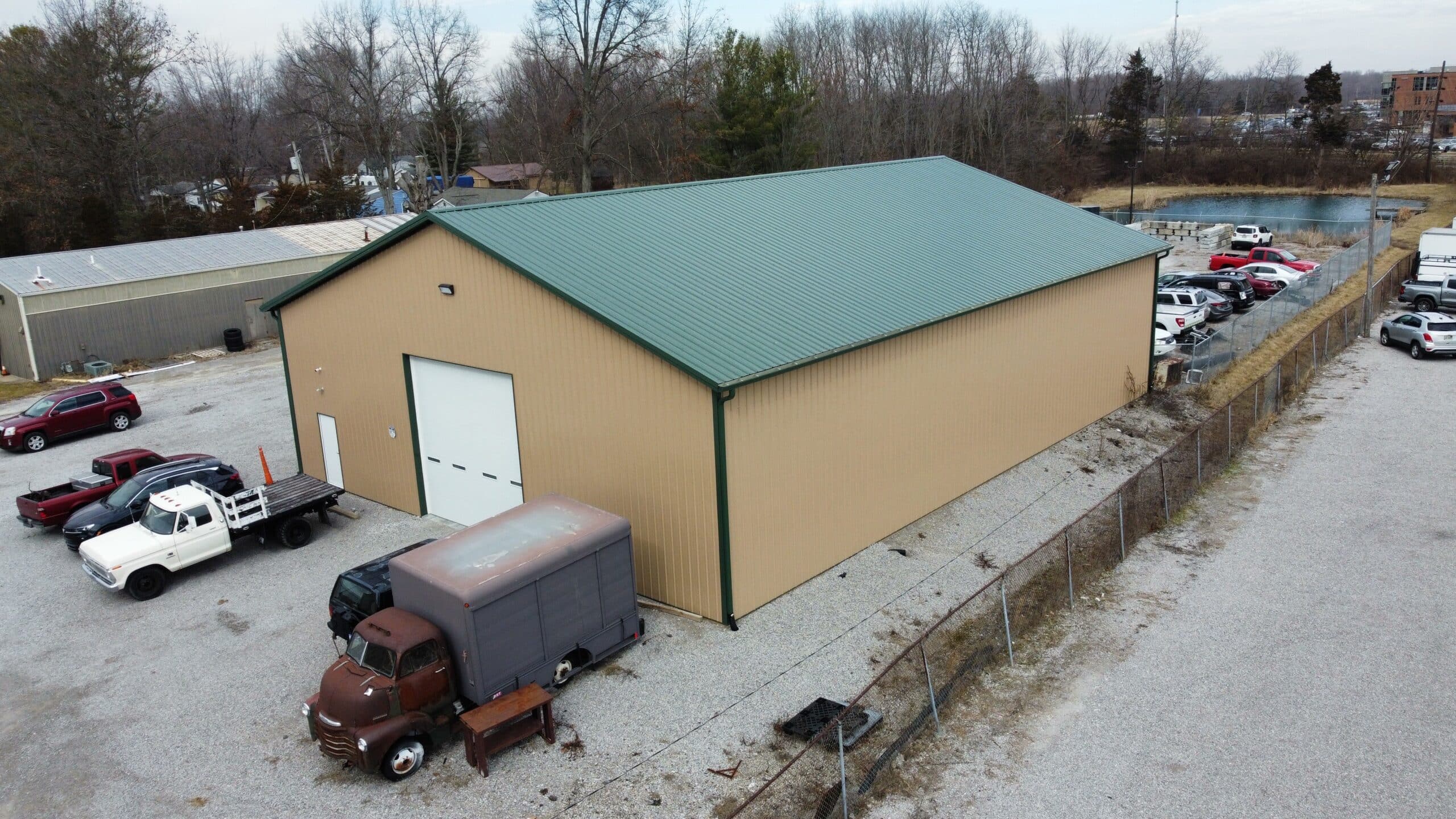 a beige 25x50 commercial pole barn with a green roof, and trucks parked outside