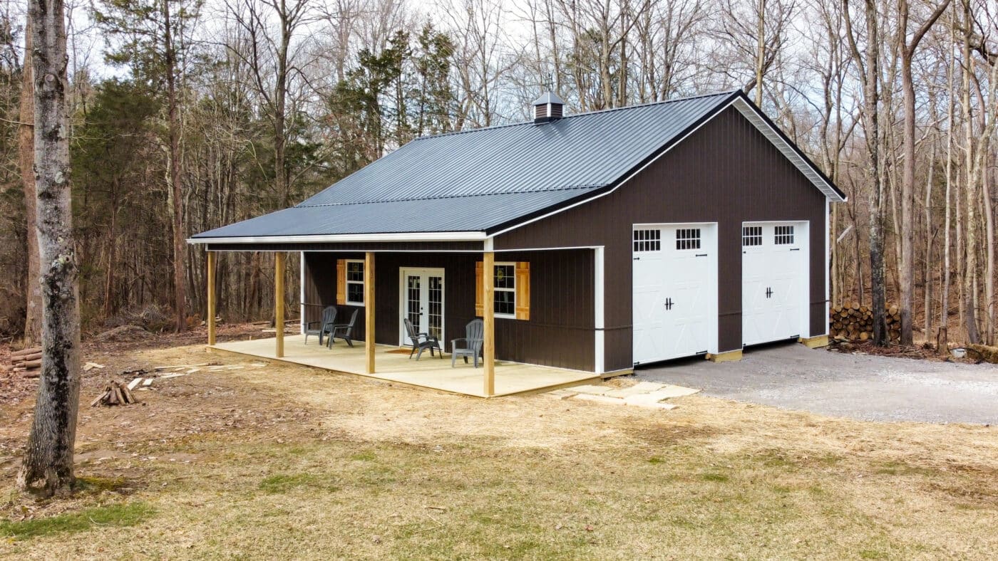 brown pole barn with black metal roof and overhang over front porch with one white garage door on the right side
