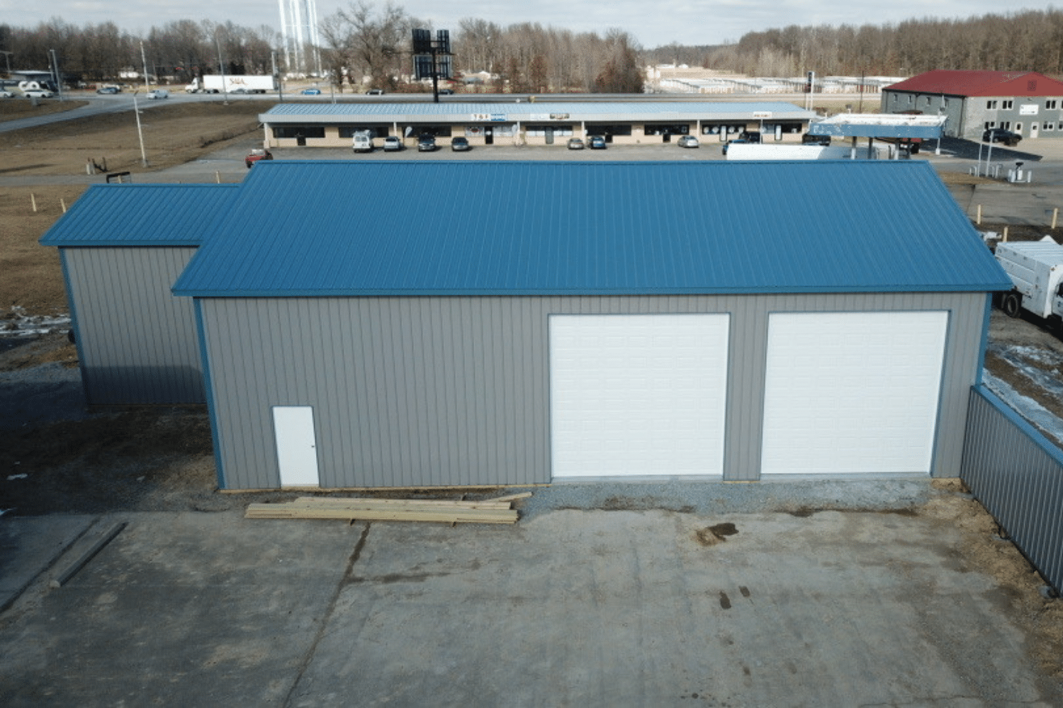 60x80 grey garage pole barn kit with blue roof and extended section and two garages with entry door on the side