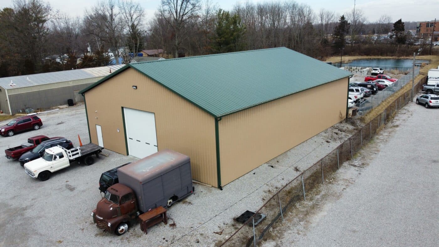 A tan 80x120 commercial pole barn with a green roof and trucks parked outside