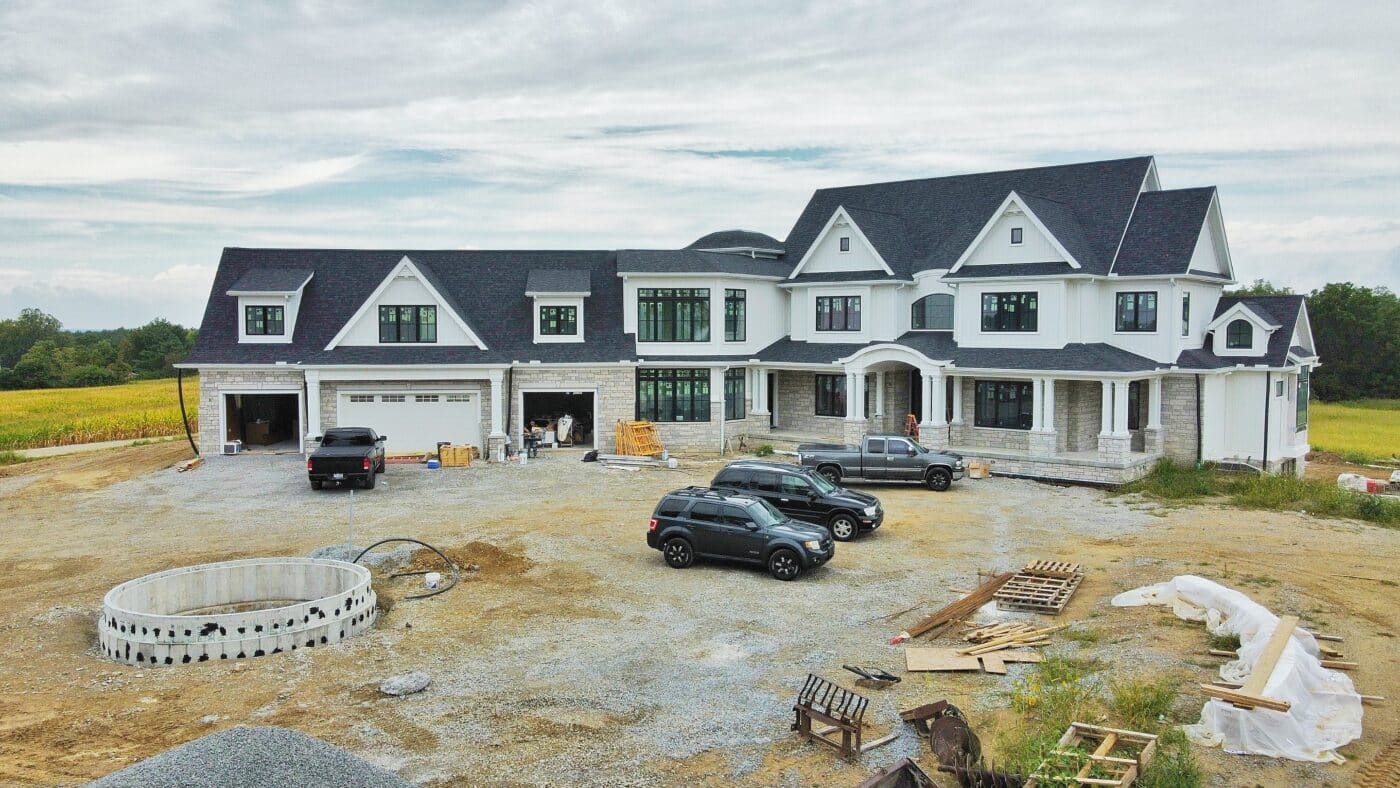 a large white home with a dark shingle roof, many windows, 4 vehicles parked outside and a man working near the garage in Jeffersonville OH