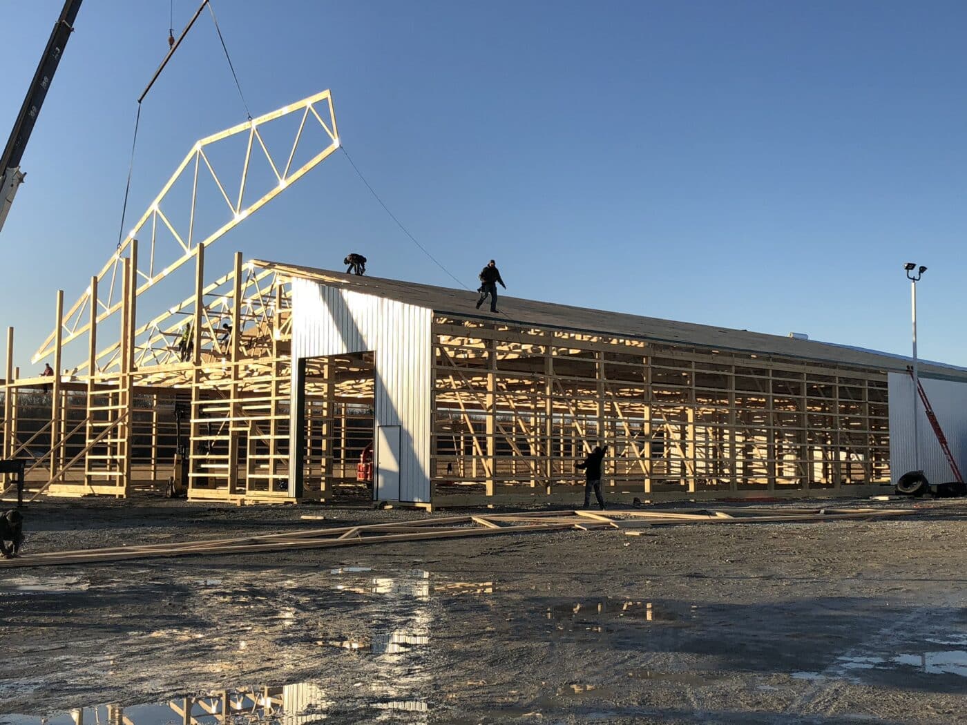 a crane lowering a roof truss onto a 25x50 commercial pole barn under construction