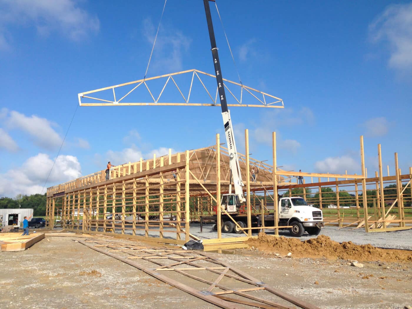 A crane lowering trusses onto a 30x70 agricultural pole barn under construction