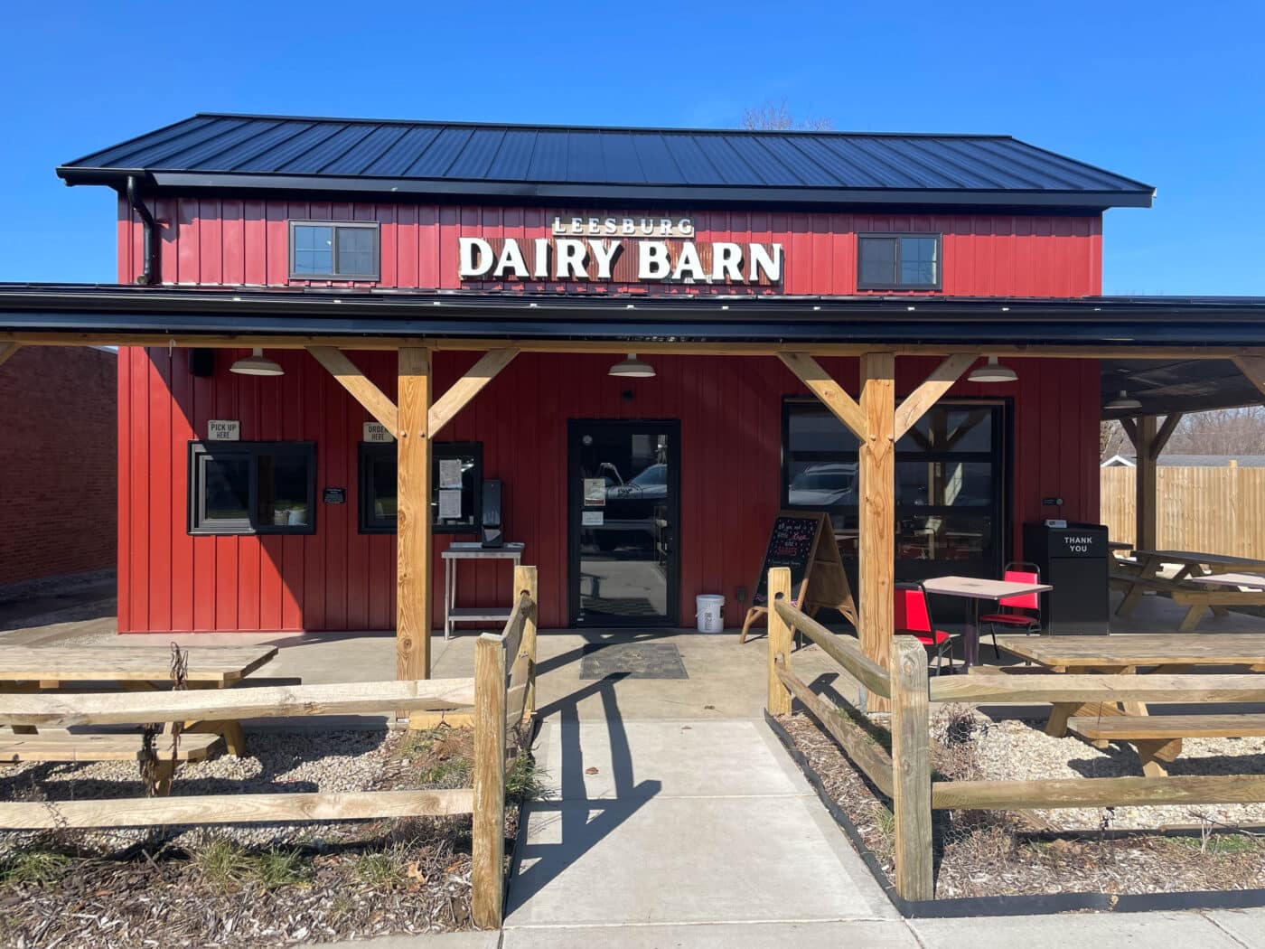 the front of a red metal dairy barn with a porch, wooden fence, and a black metal roof in leesburg OH