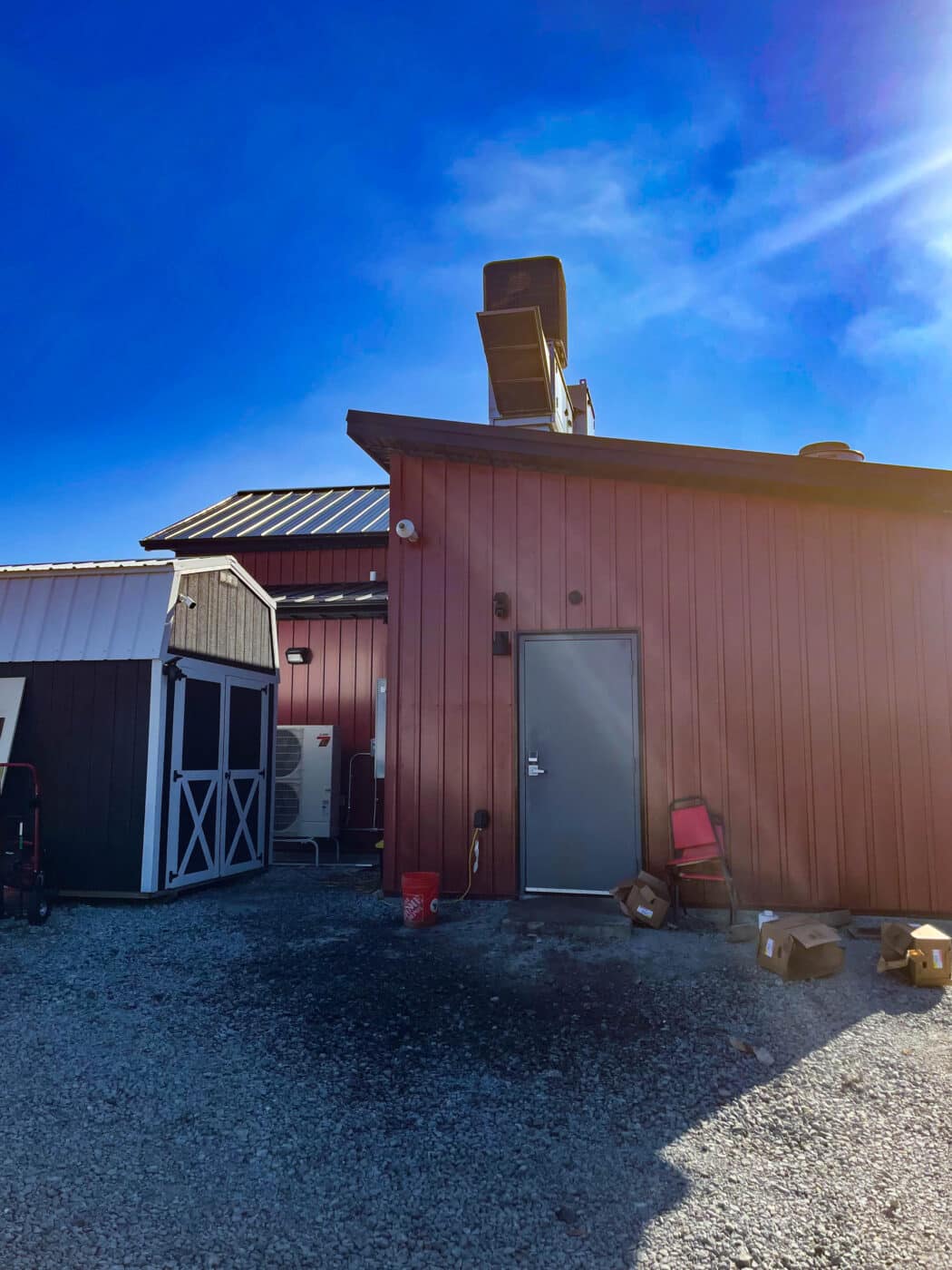 the back door to the red metal dairy barn that leads out to a lot with a grey shed