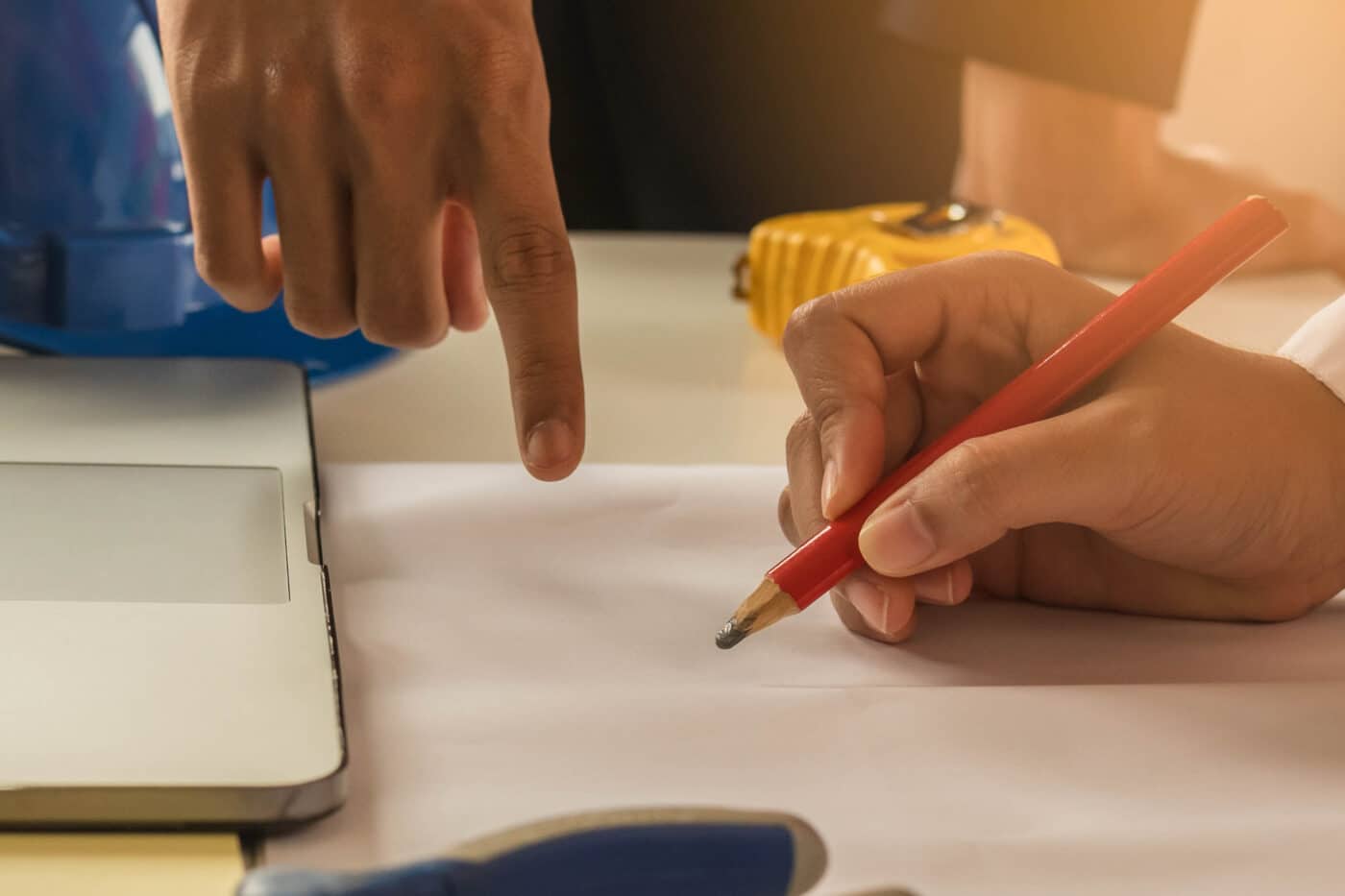 two people drawing the design for a 20x48 barndominium kit with pencil and paper
