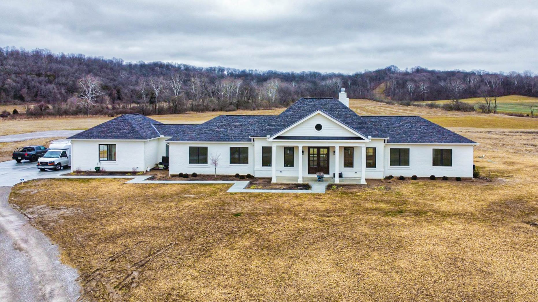 A white 75x100 barndominium with a grey shingle roof in a field