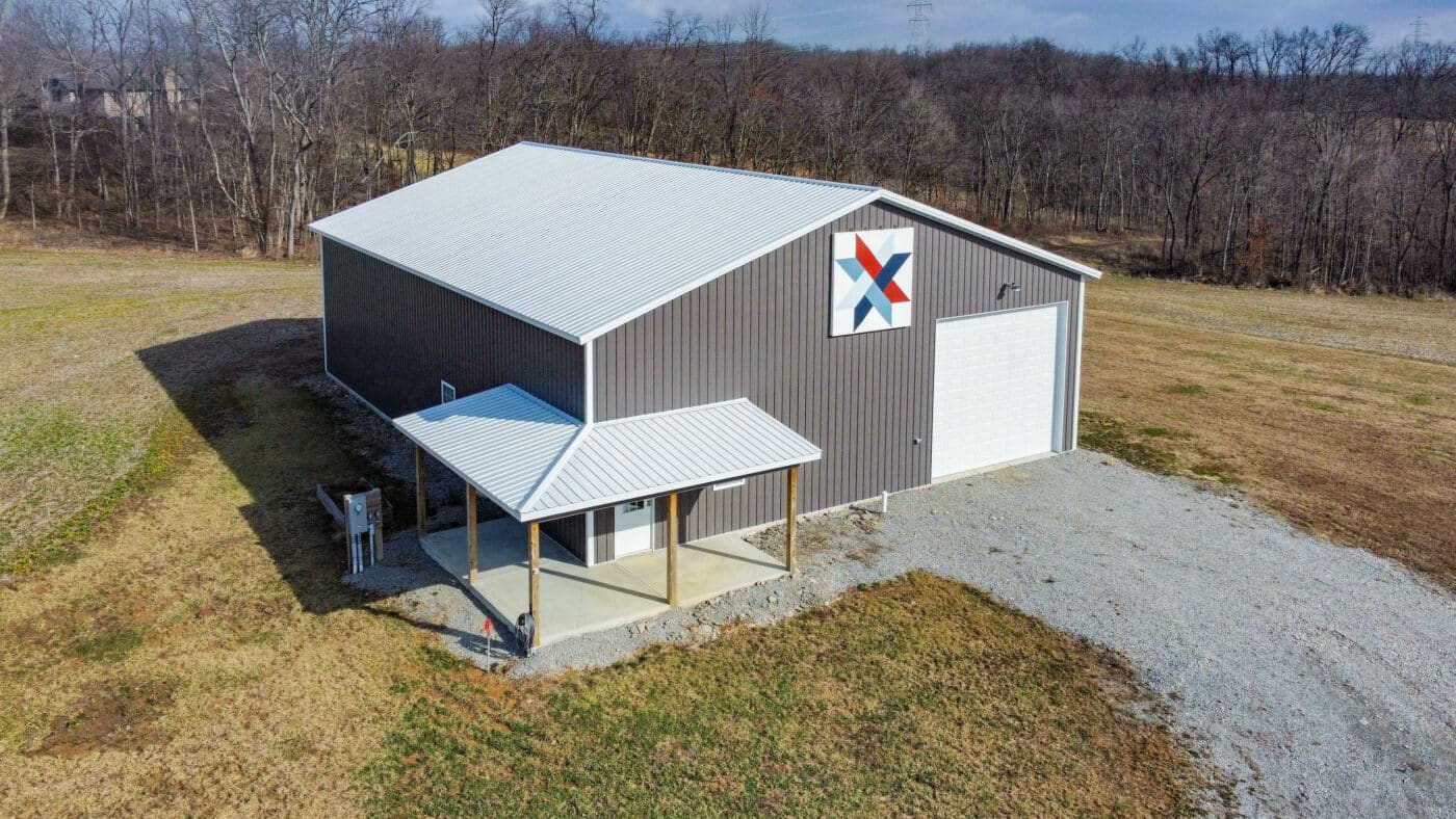 gray metal 36x48 pole barn garage with whitish gray metal roofing barn star on top and one white overhead door featuring white entry door with white:gray metal overhang over it