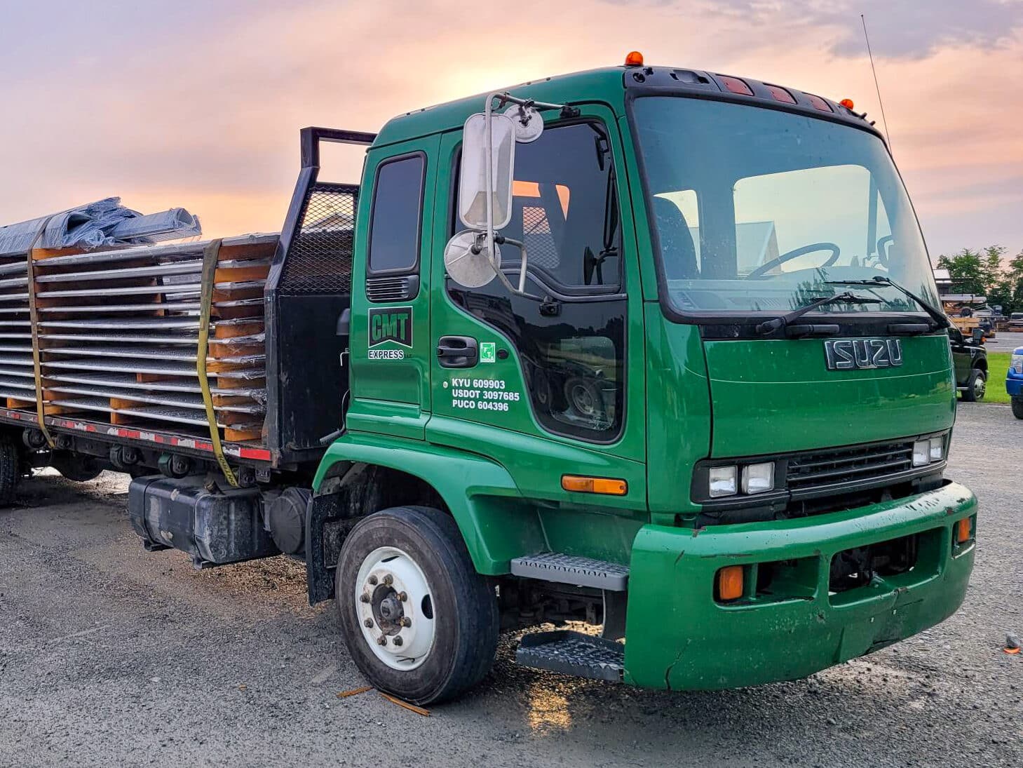 green truck with metal panels strapped to trailer bed ready to deliver them to a 40x100 agricultural pole barn job site