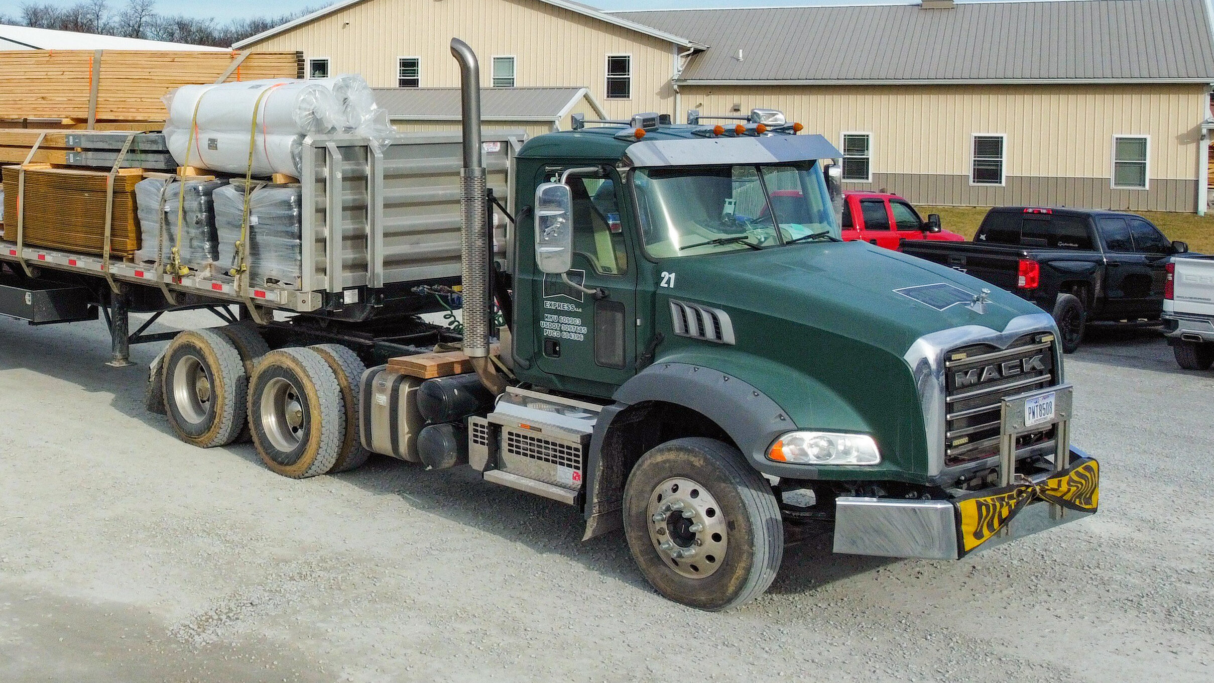 green truck with wooden roof trusses and metal building components strapped to back driving to deliver a 36x60 agricultural pole barn kit to its job site