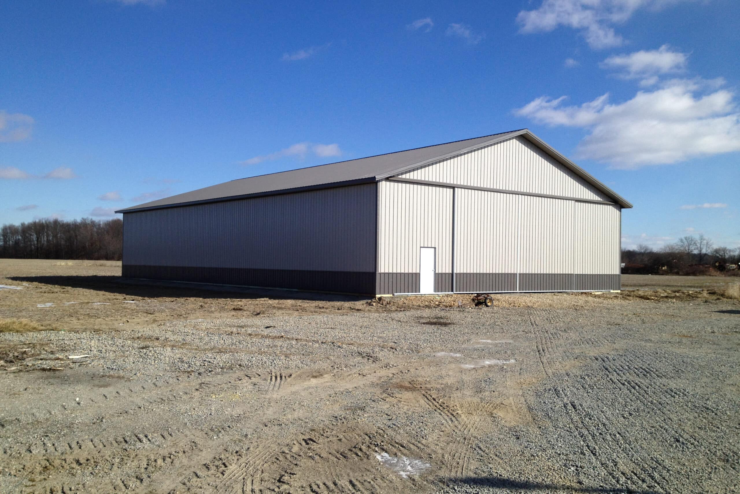 light gray pole barn with dark gray trim and metal paneling along bottom and dark gray metal roof featuring slider doors