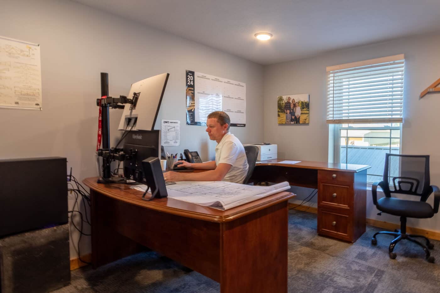 man sitting at desk work on computer with blueprints for a 30x50 pole barn garage sitting in front of him