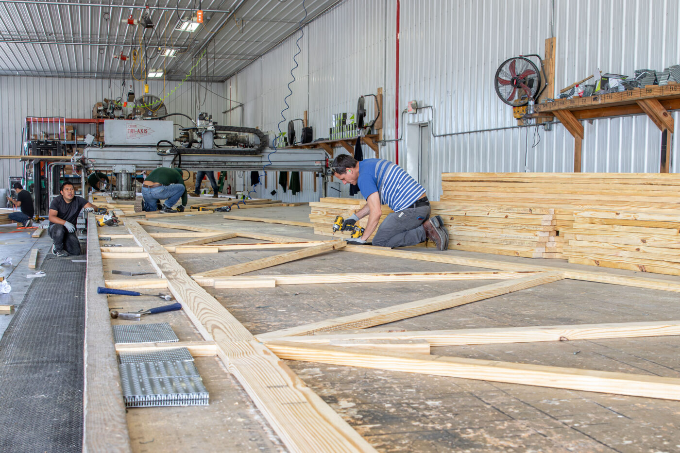 men working together to screw together pieced of lumber to manufacture a wooden roof truss