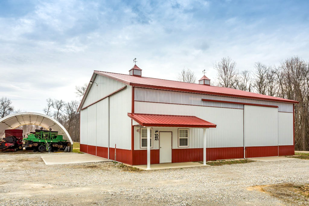 red and white agricultural pole barn with two cupolas slider door and side entry door with red overhang over it plus a little additional area for equipment storage