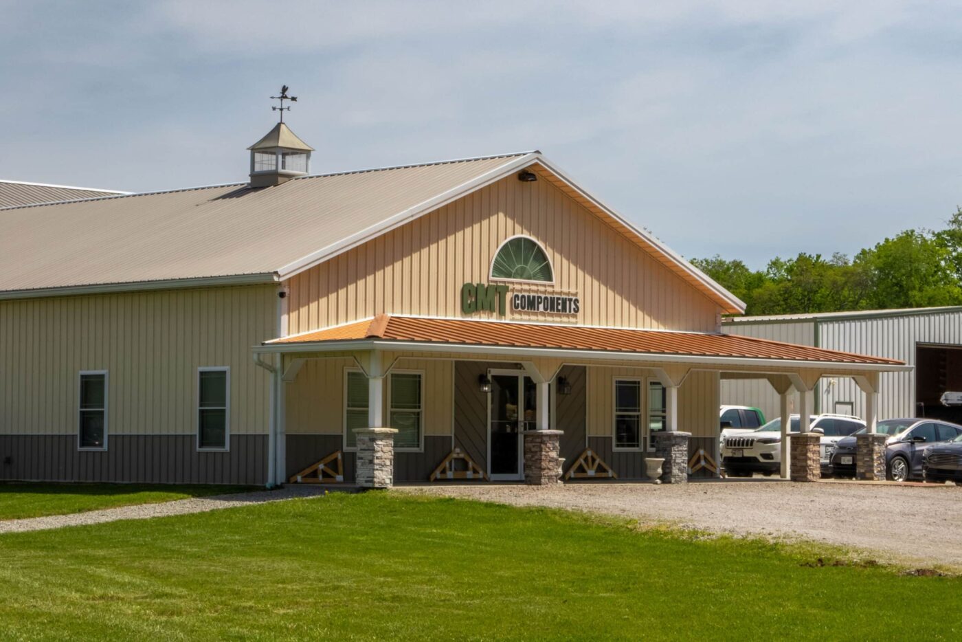 tan CMT components building with overhang with orange metal panels featuring cars parked out front