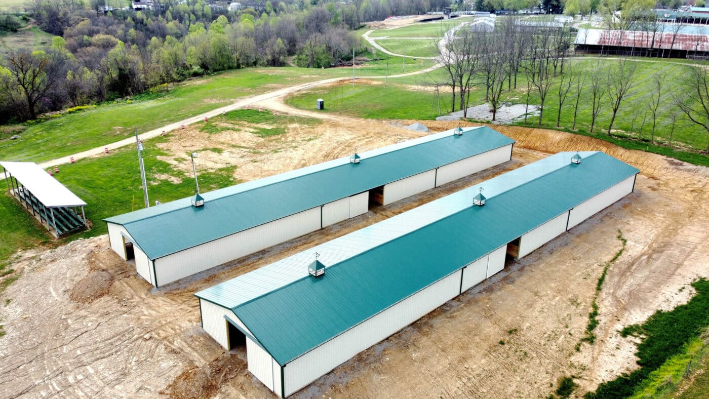 aerial view of two 60x80 agricultural pole barns with tan metal siding green trim and green metal roofing on fair grounds