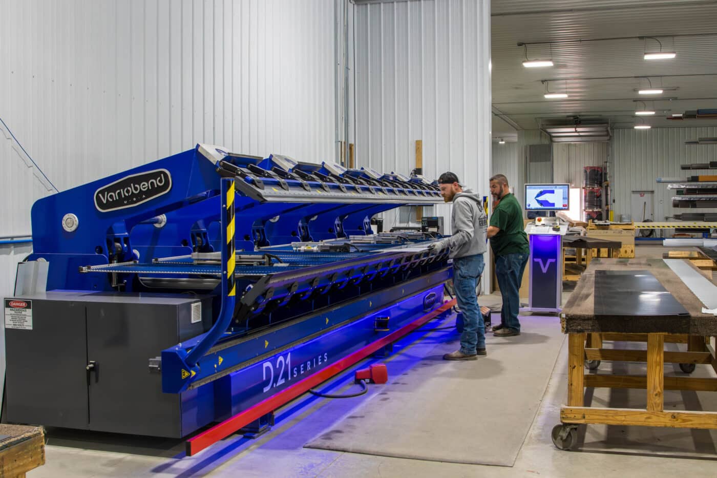 two men cutting metal panels at blue machine