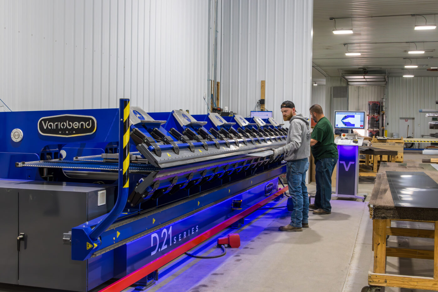 two men placing metal panels into blue machine and custom cutting them to the measurements of a 40x100 agricultural pole barn kit