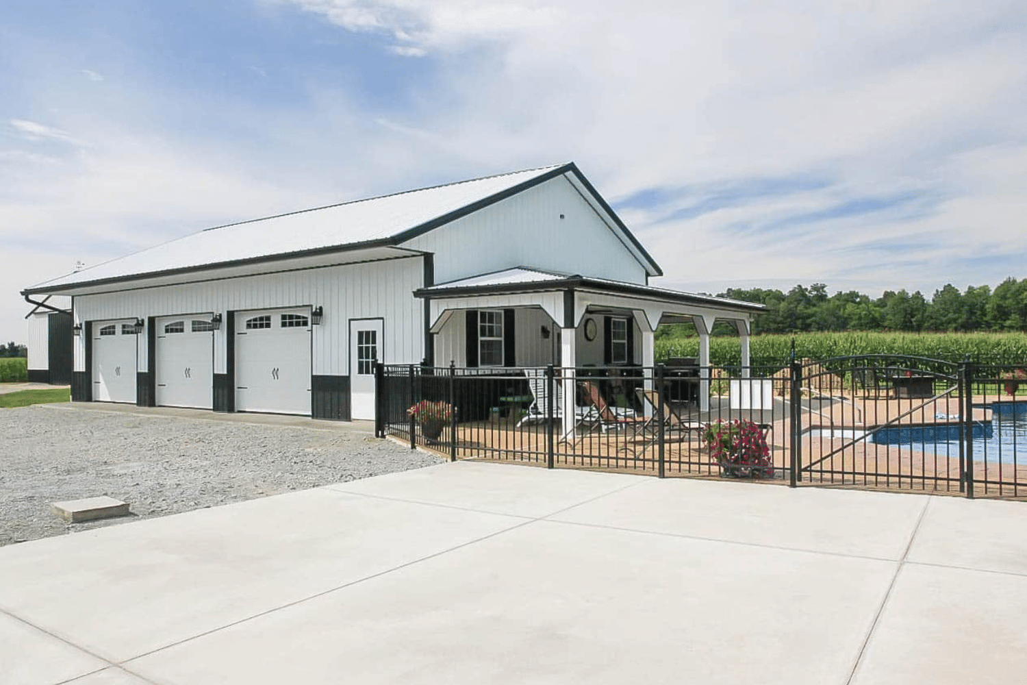 white 50x50 barndominium with three white garages and porch next to pool