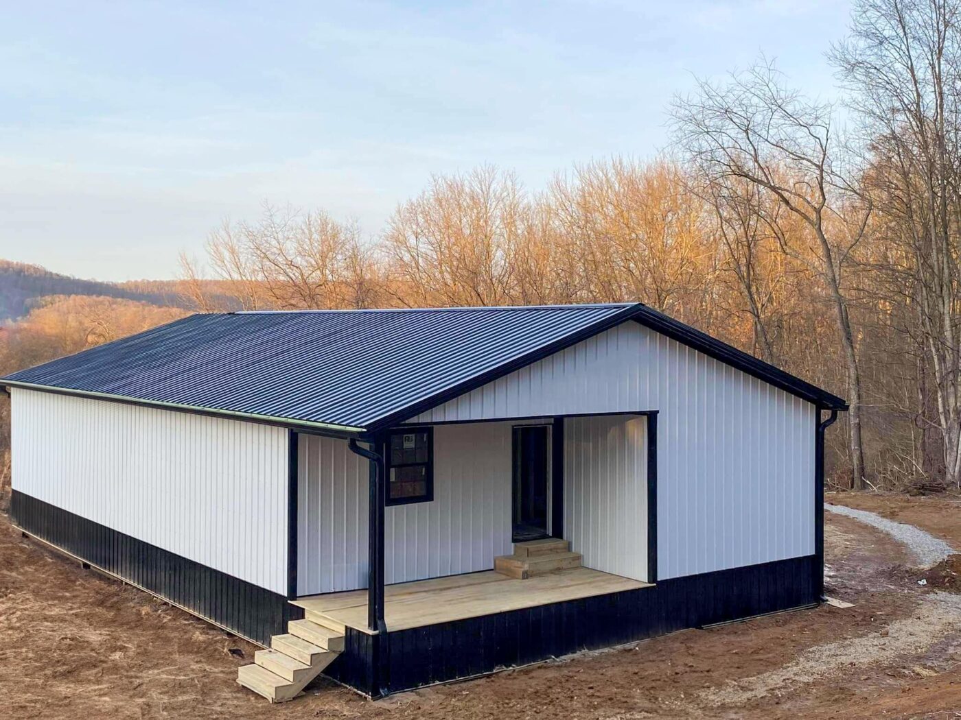 a white 20x48 barndominium with black trim and a black roof and a front porch