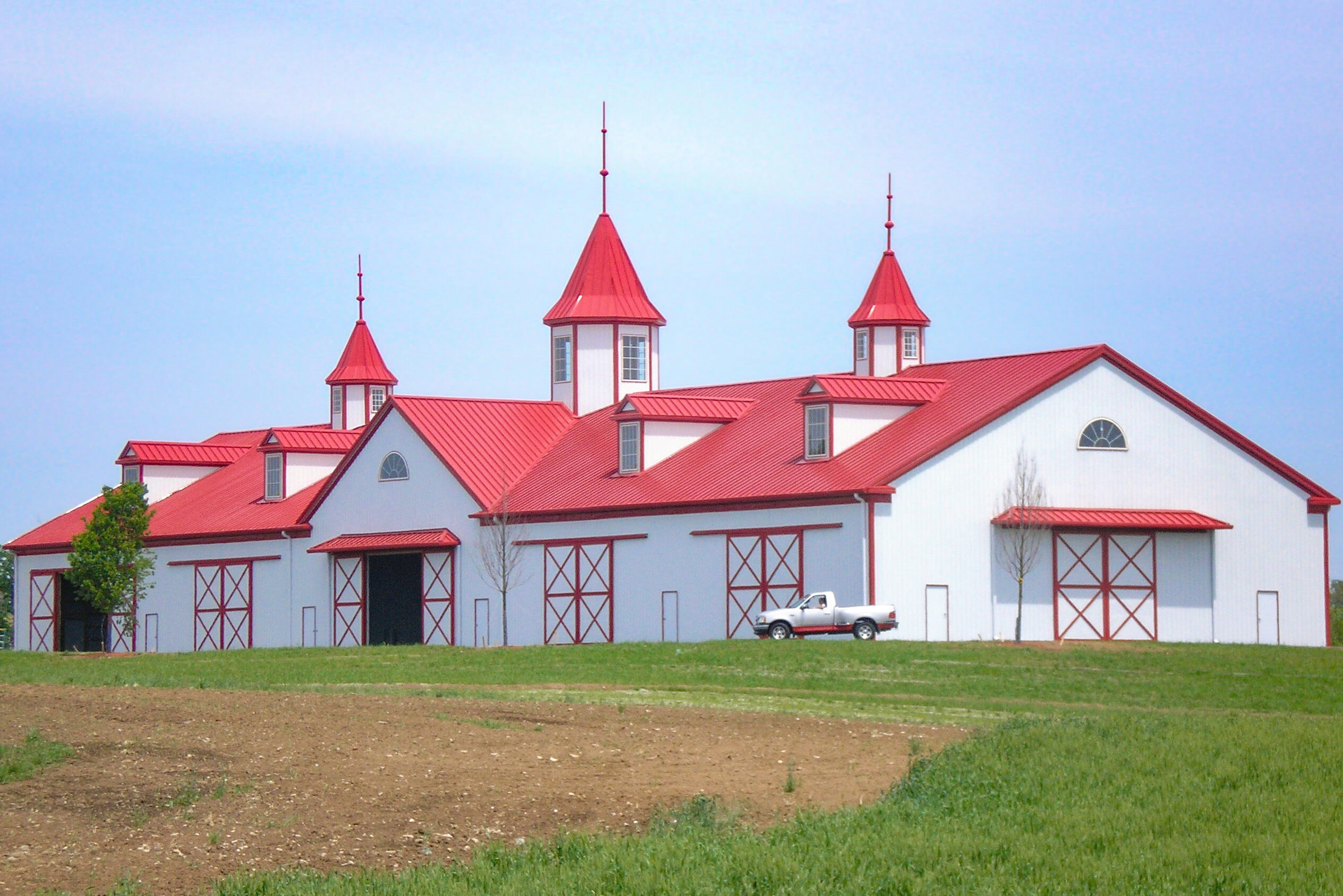white and red trimmed 40x100 agricultural pole barn with red metal roof and three white and red towers coming out of the roof featuring multiple slider doors and dormers